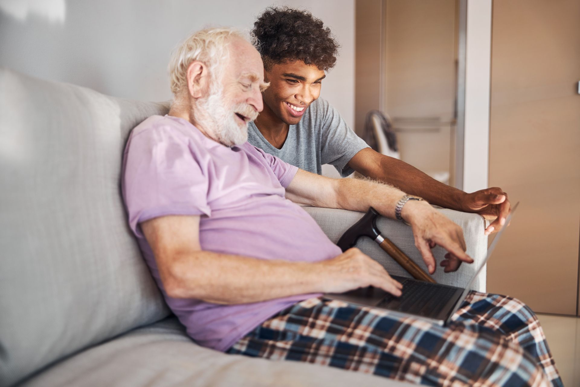 An older person and a younger person looking at a laptop together on a couch; both smiling.