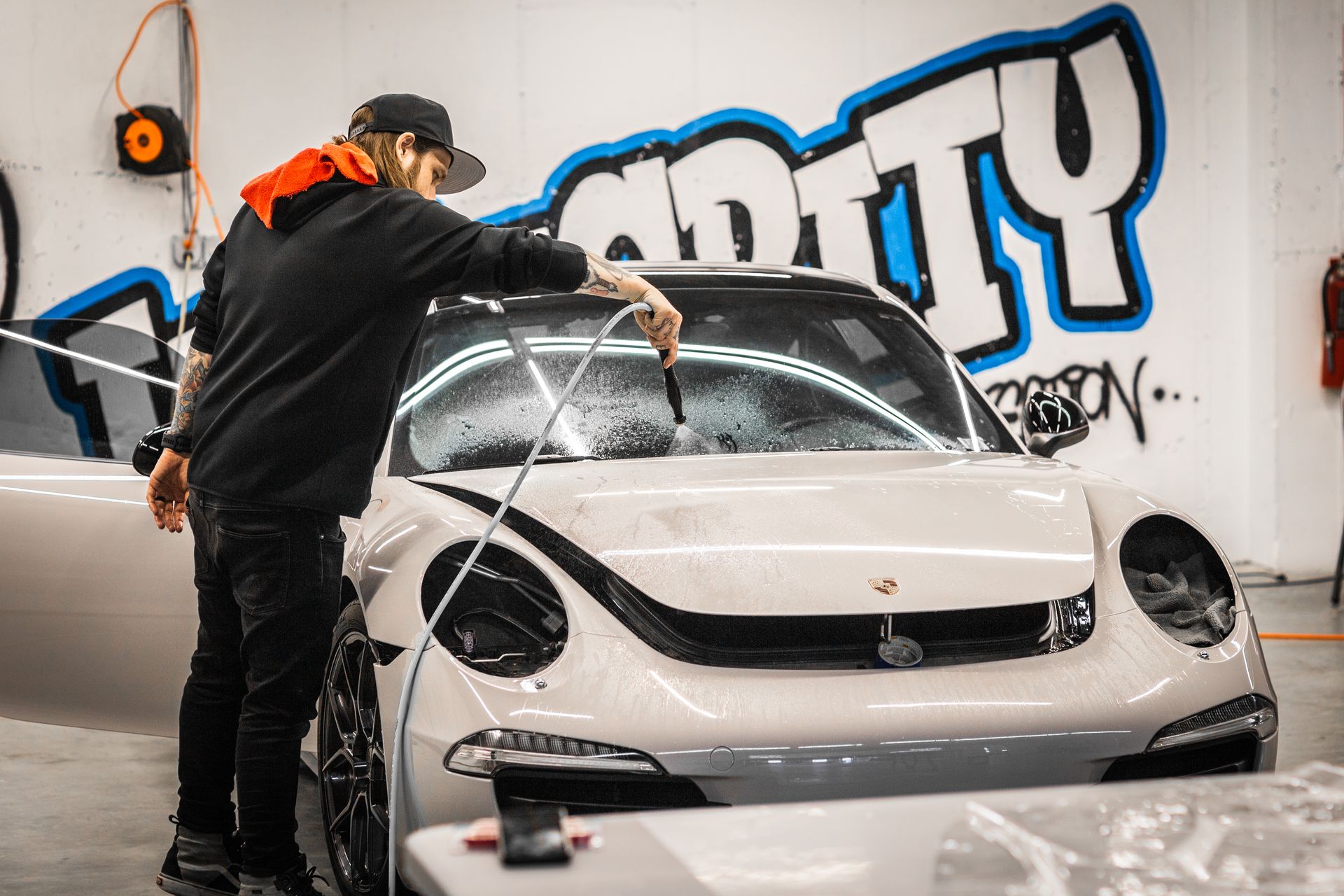 A woman is wrapping a car with plastic wrap in a garage.