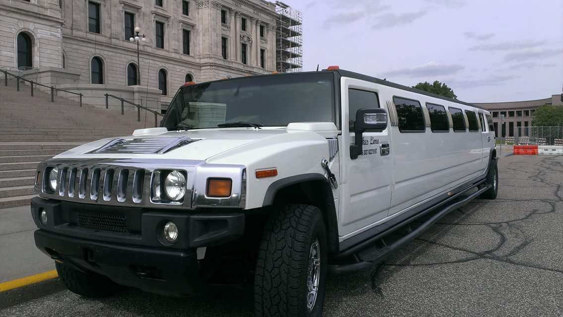 A white hummer limousine is parked in front of a building.