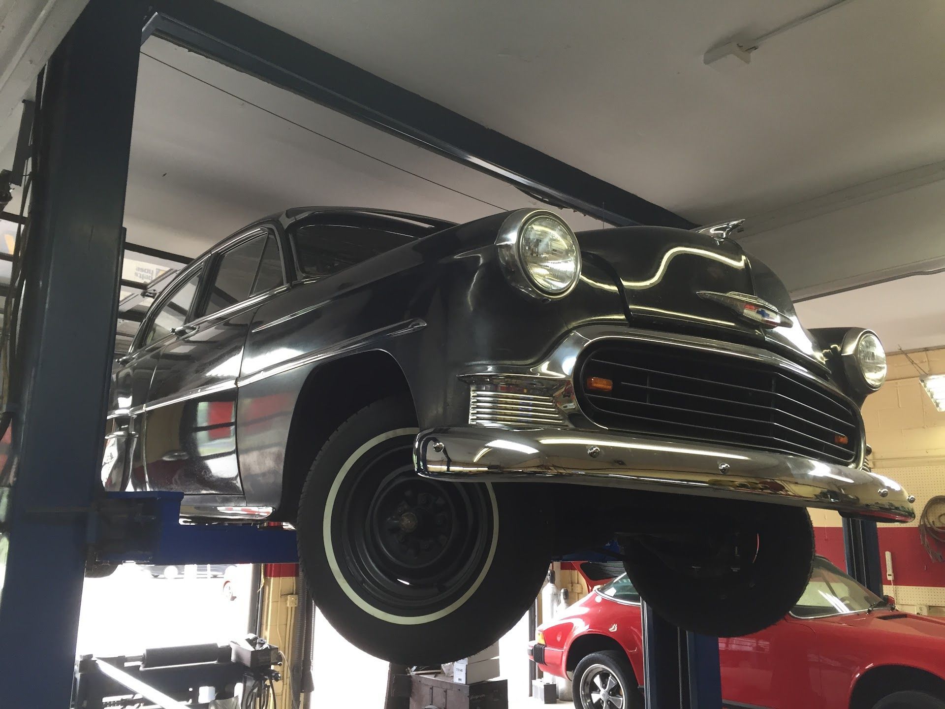 Black classic car on a lift in a garage, with a red car visible in the background. | Rose Brothers Garage
