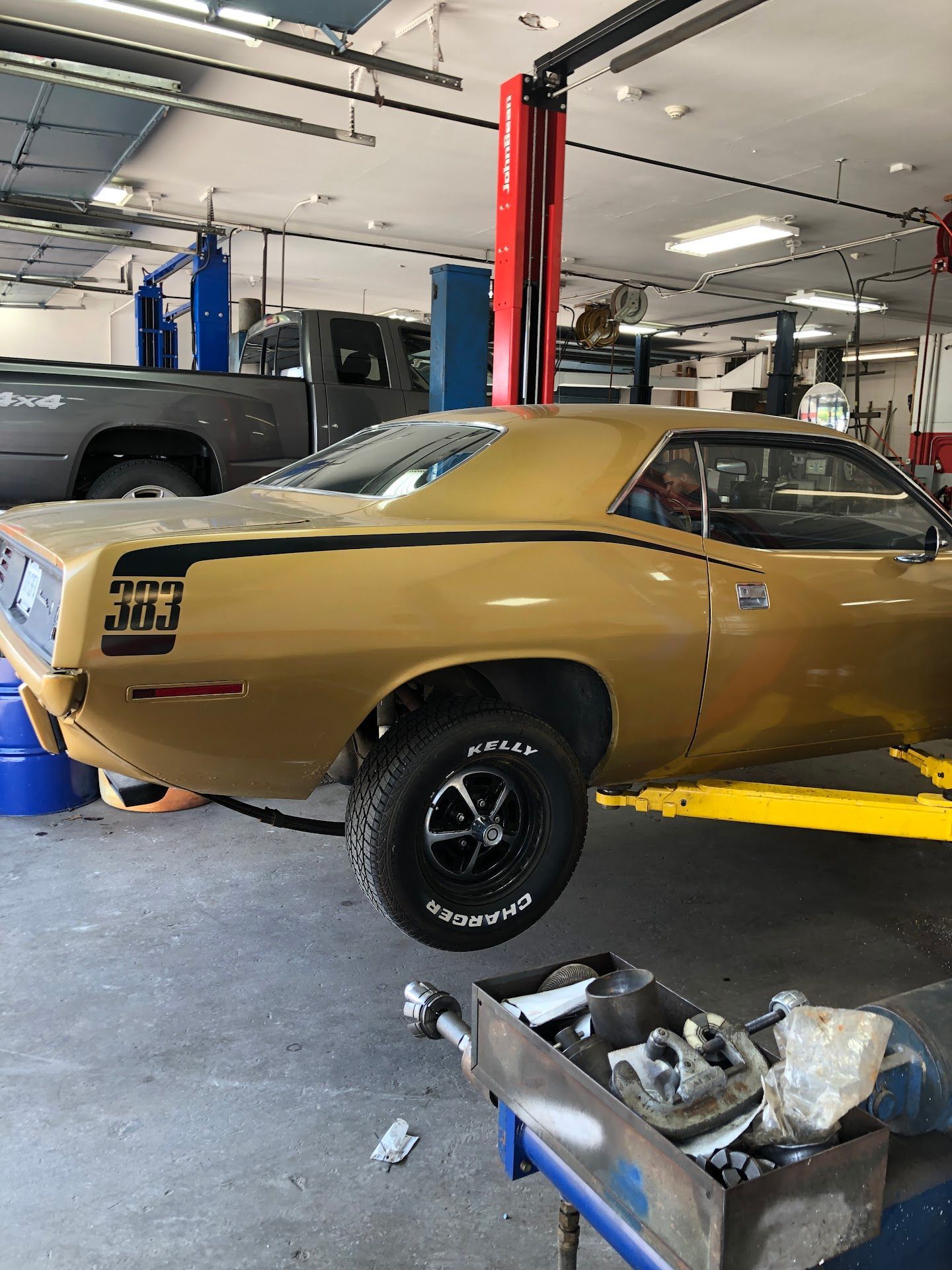Gold muscle car on a lift in an auto repair shop, with a
