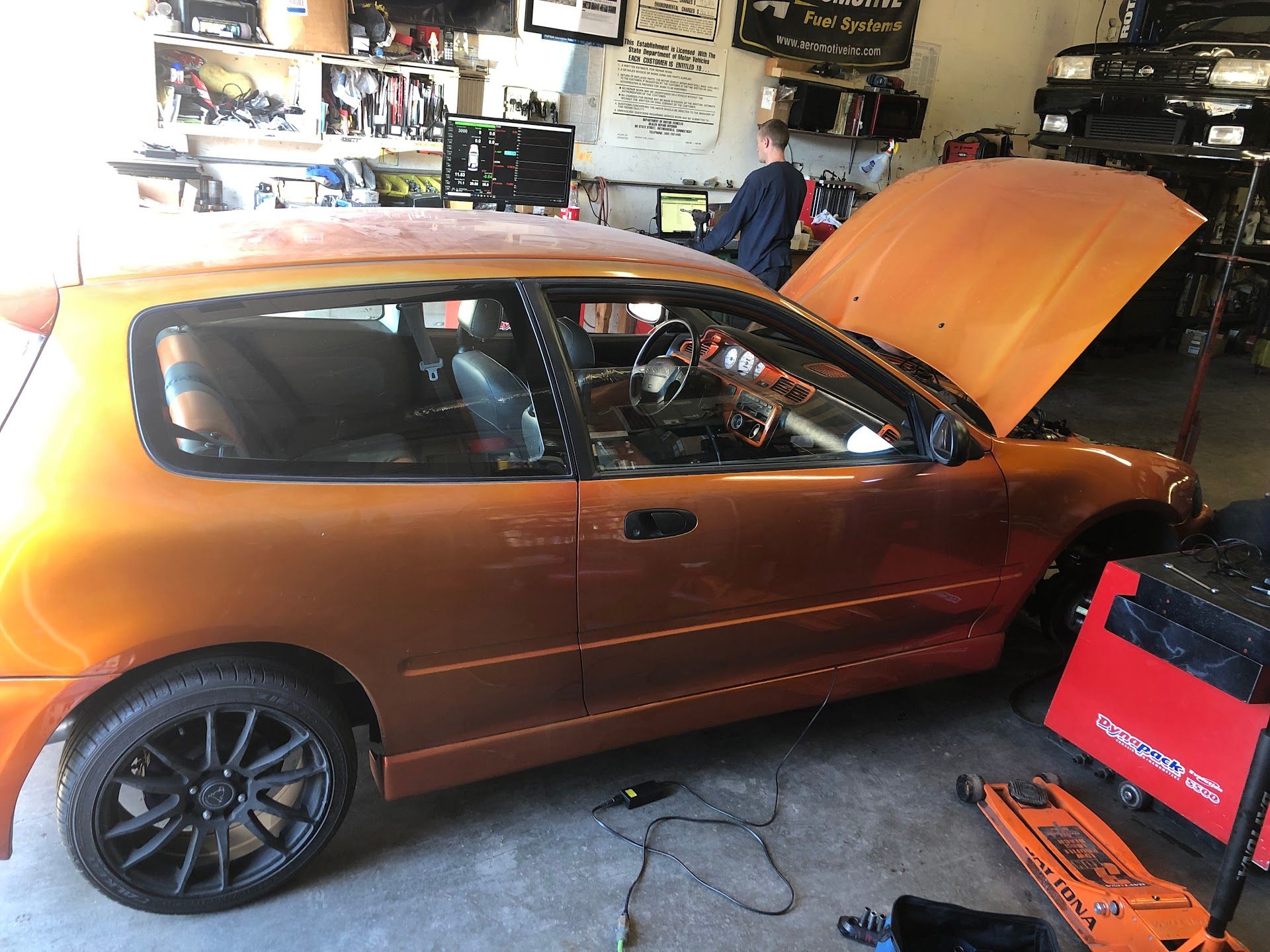 Orange car with hood open in garage. A person is near a computer. | Rose Brothers Garage