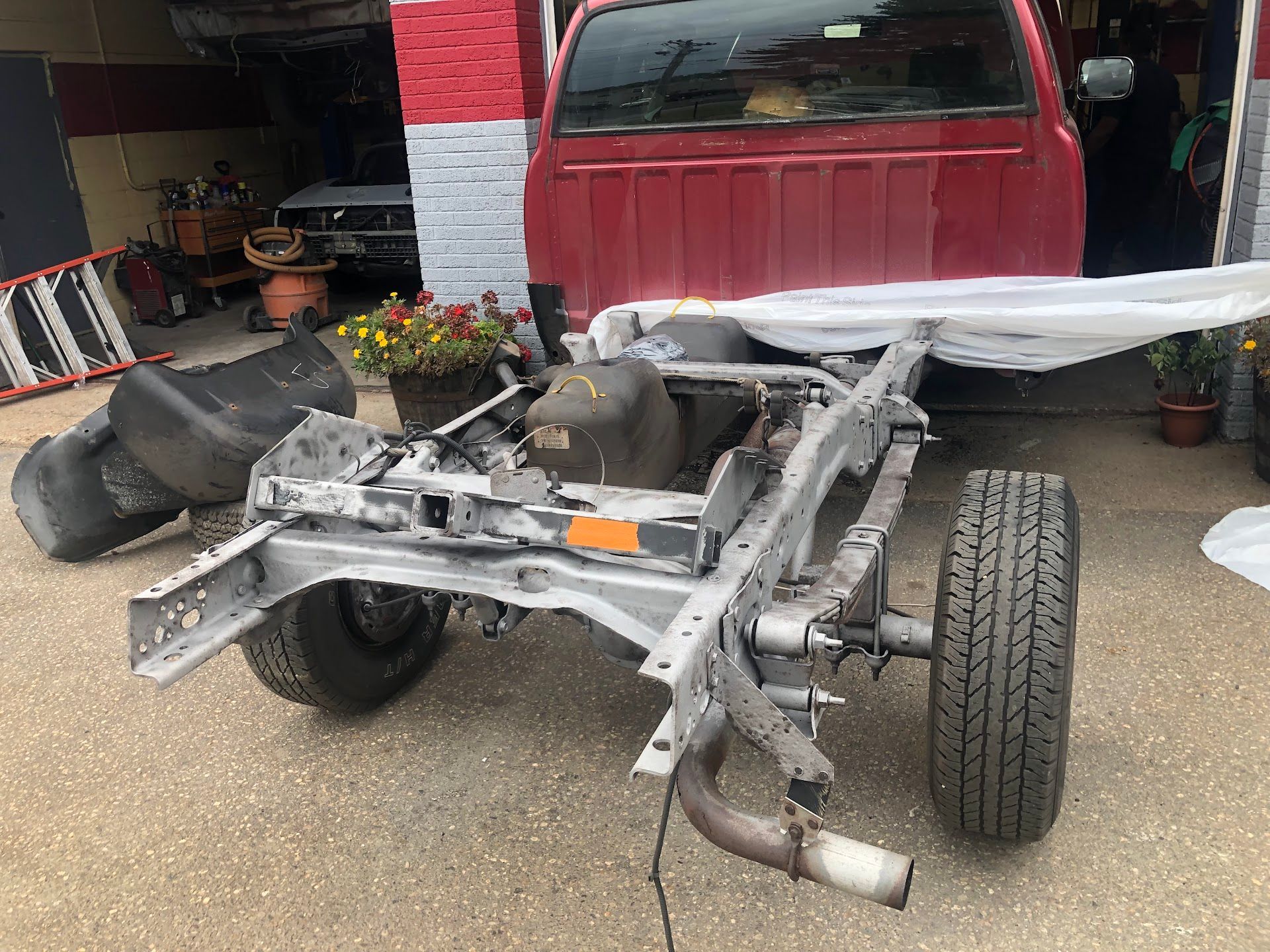 Red truck bed over a bare, gray truck frame. Tires and other parts scattered on pavement in a garage. | Rose Brothers Garage