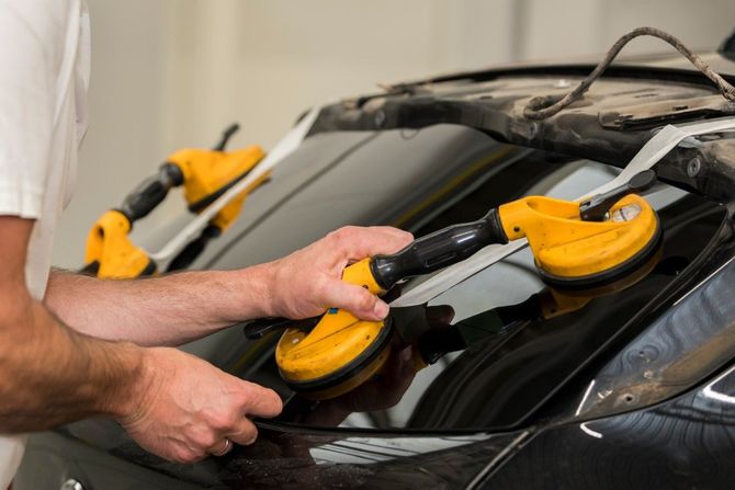 Worker using a yellow suction lifter to remove glass from a black car windshield