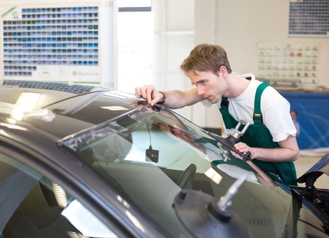 Mechanic inspecting a car windshield in an auto shop, using a tool on the glass.