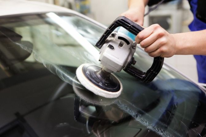 Person polishing a car windshield with a power buffer, creating a glossy finish.
