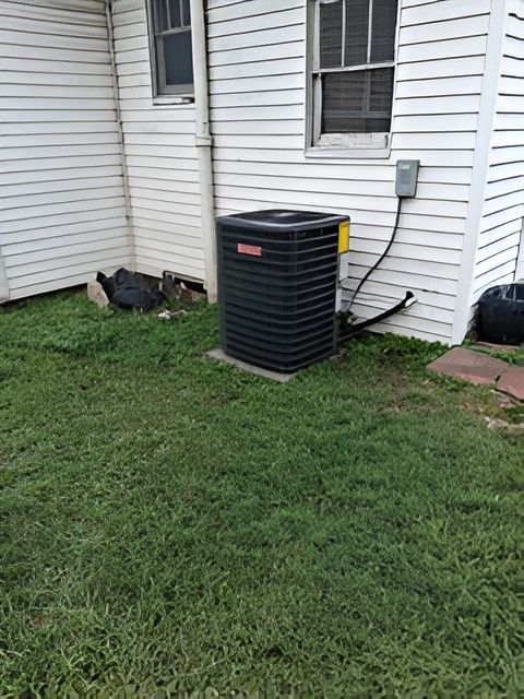 Air conditioning unit next to a white house with windows, sitting on a concrete slab in grass.