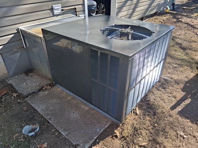 Gray air conditioner unit outside a building, set on concrete pads.