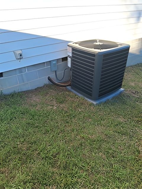 An air conditioning unit next to a light-colored building with a grass lawn.