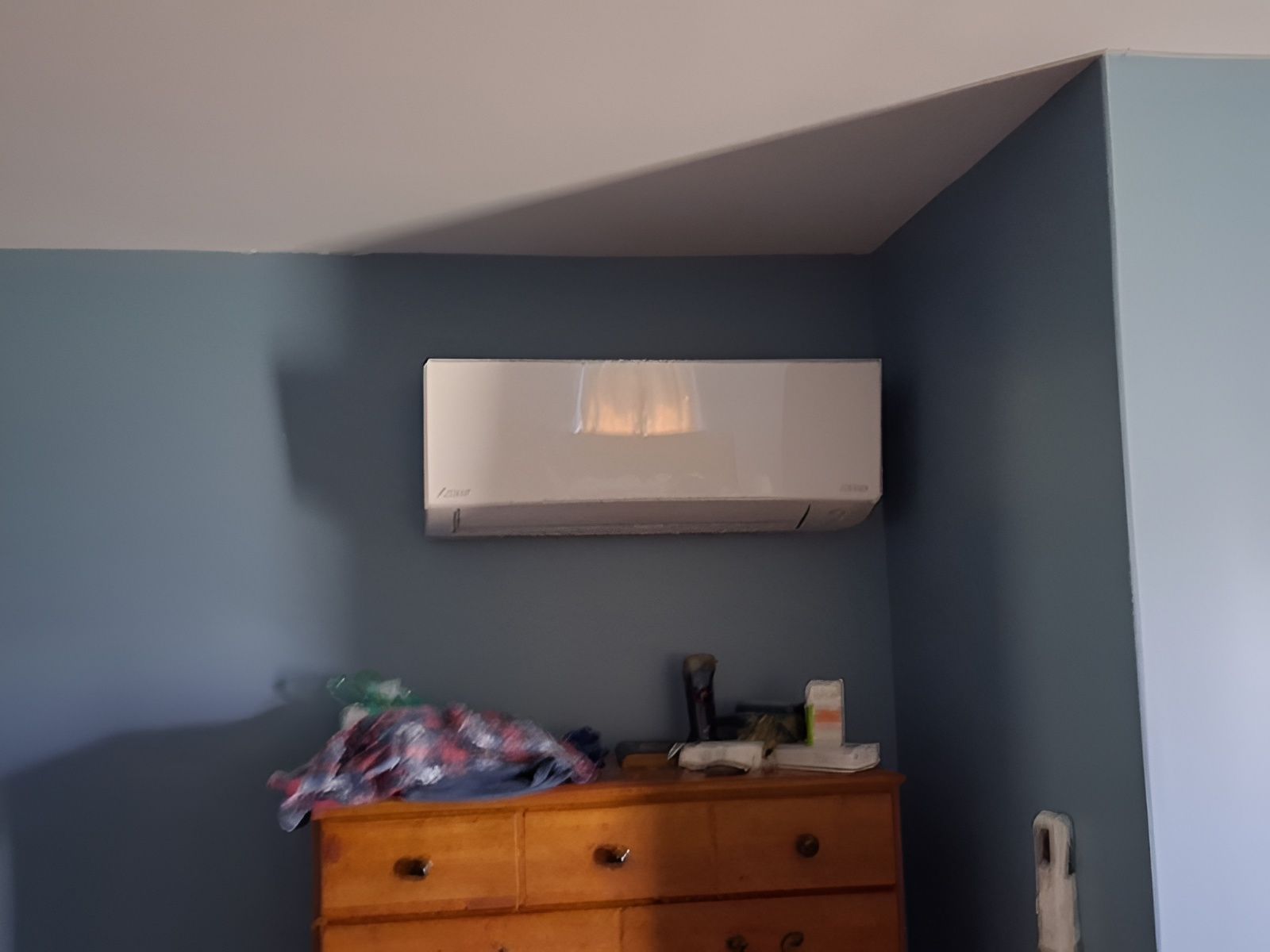 White air conditioner mounted on a blue wall above a wooden dresser.
