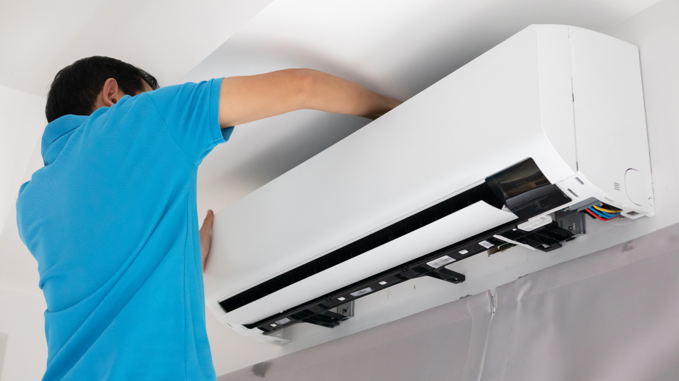 Person in blue shirt installing a white wall-mounted air conditioner unit.