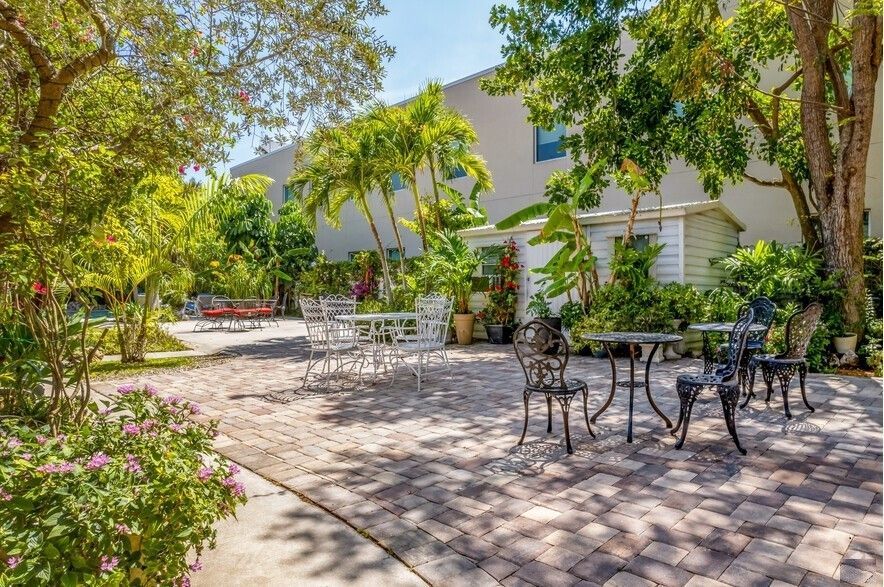 A patio with tables and chairs in front of a building surrounded by trees.