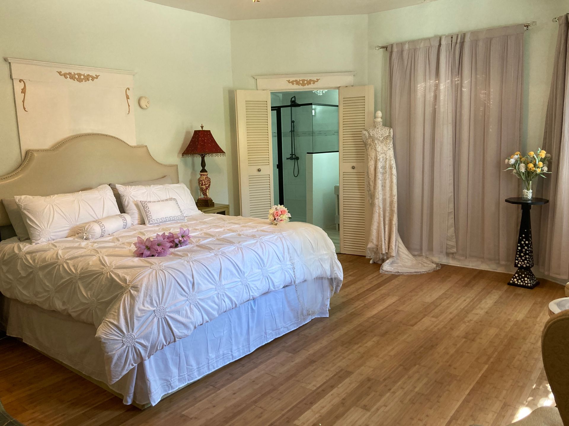 A bedroom with a large bed and a wedding dress hanging on the wall.