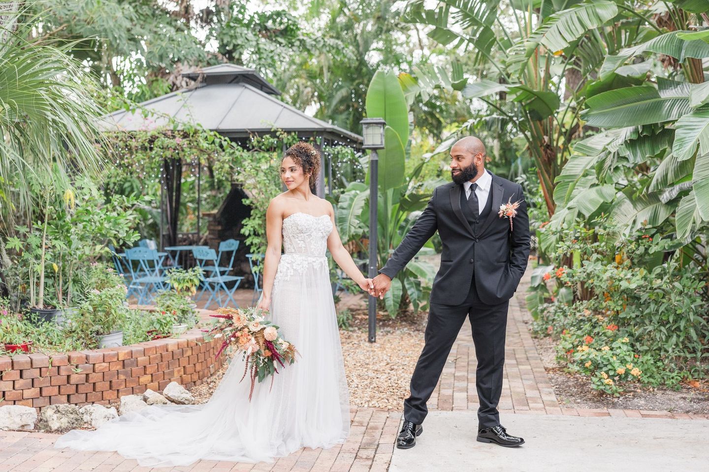 A bride and groom are holding hands in front of a gazebo.