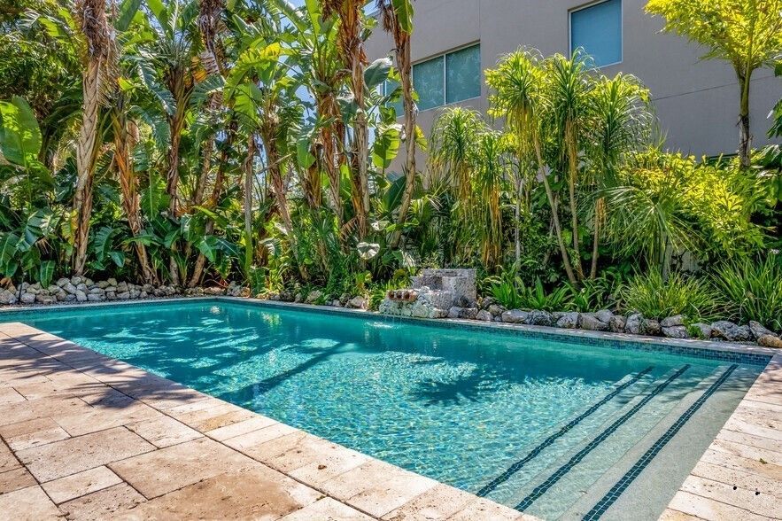 A large swimming pool surrounded by trees and bushes in front of a building.