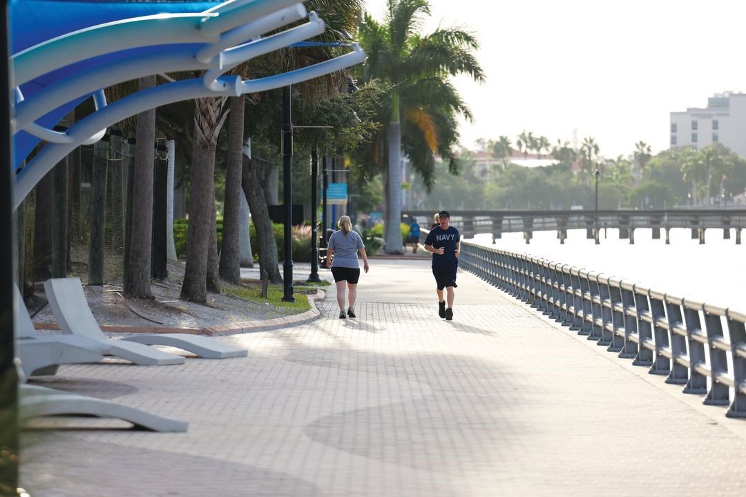Two people are jogging on a sidewalk next to a body of water.