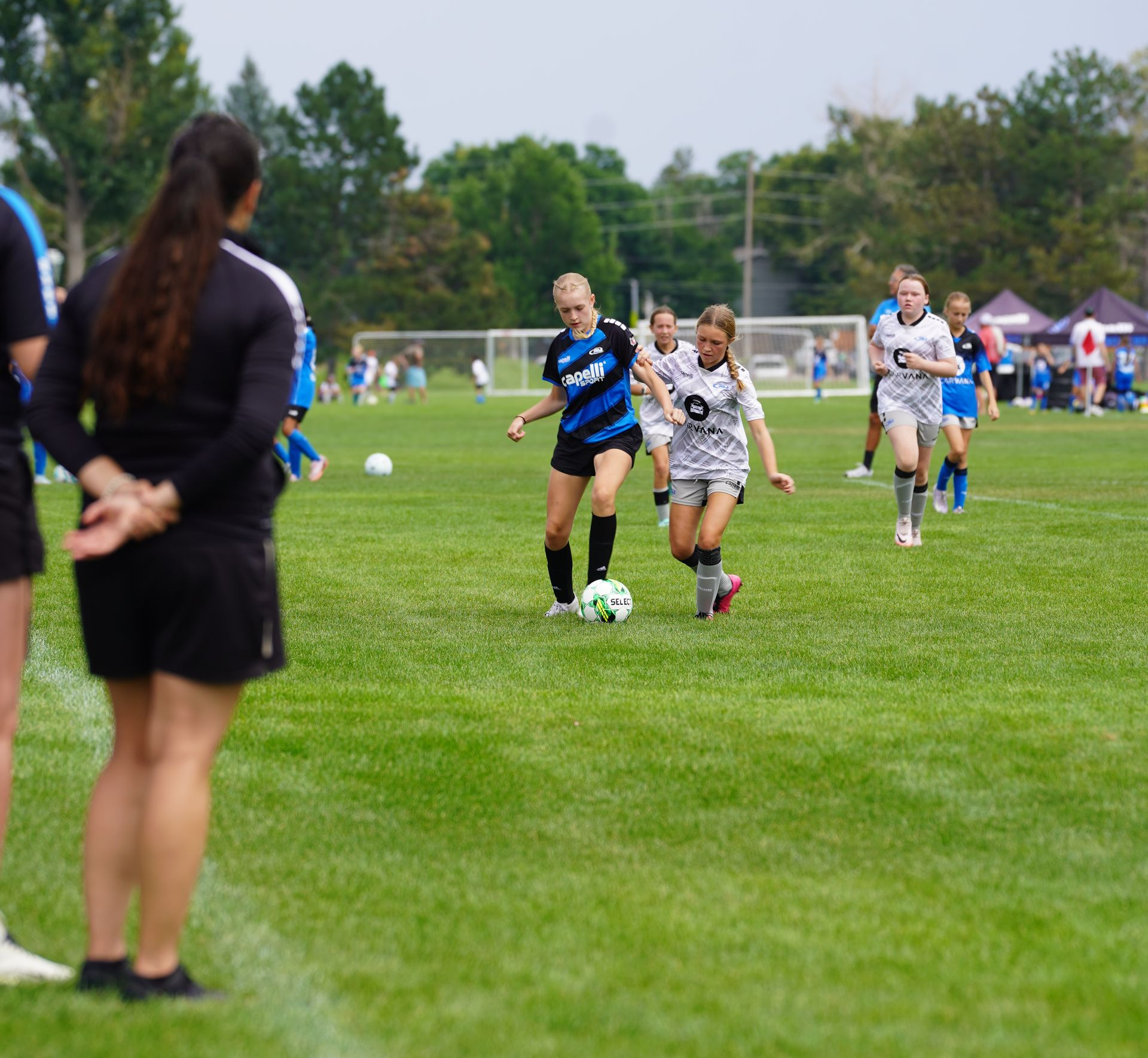Two young girls are playing soccer on a field.