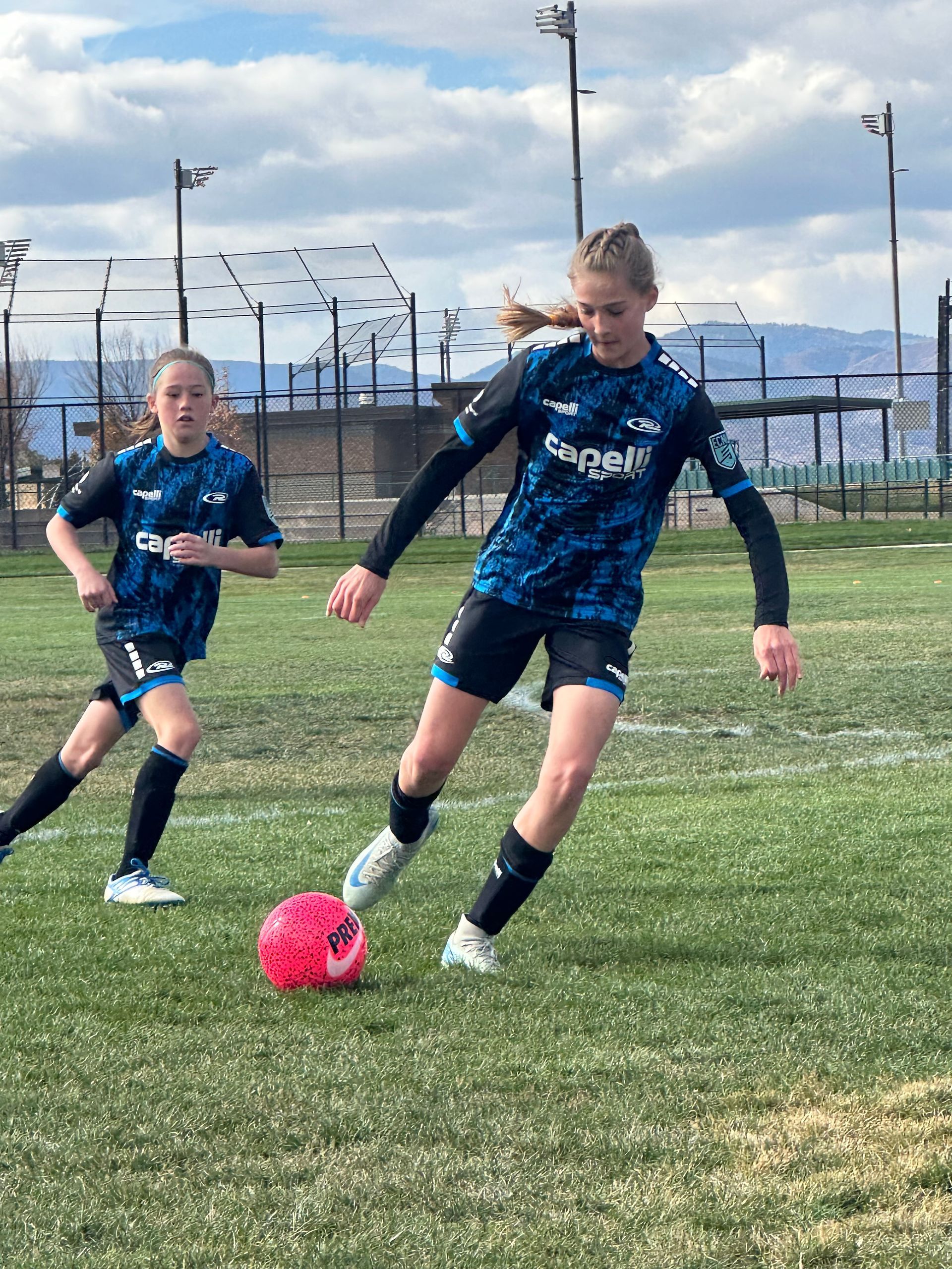 Two young girls are playing soccer on a field.