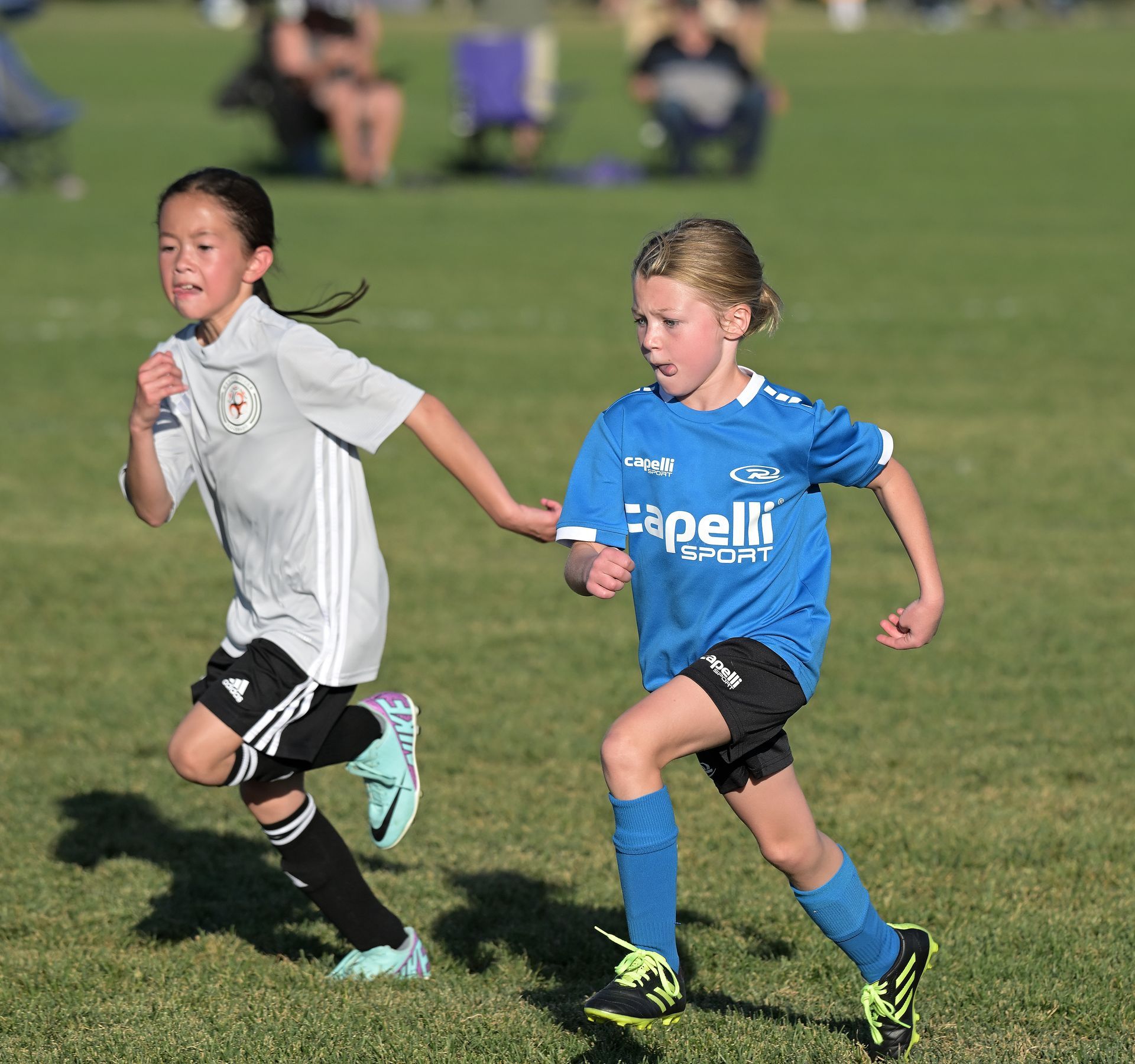 Two young girls are running on a field with one wearing a shirt that says capelli sport