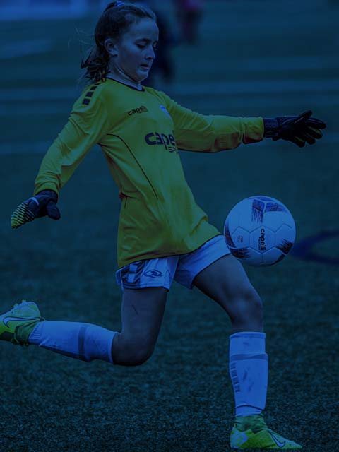 A young girl is kicking a soccer ball on a field.