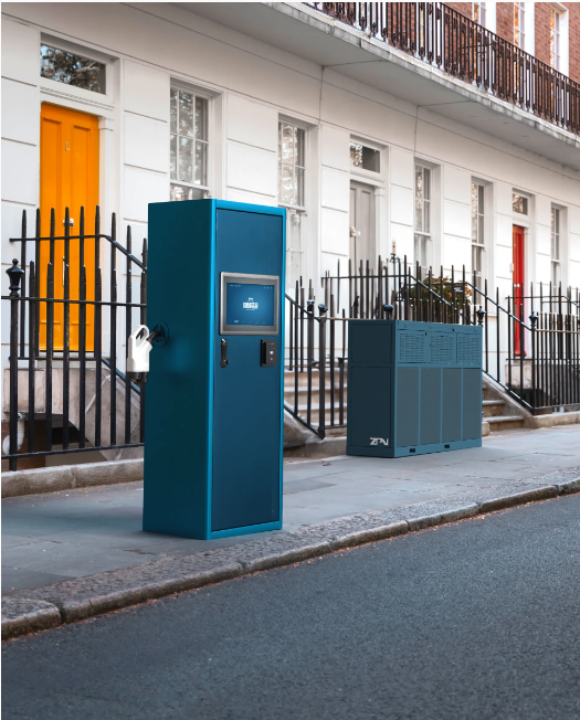 A blue box on the sidewalk in front of a building with a yellow door. ZPN Hubz