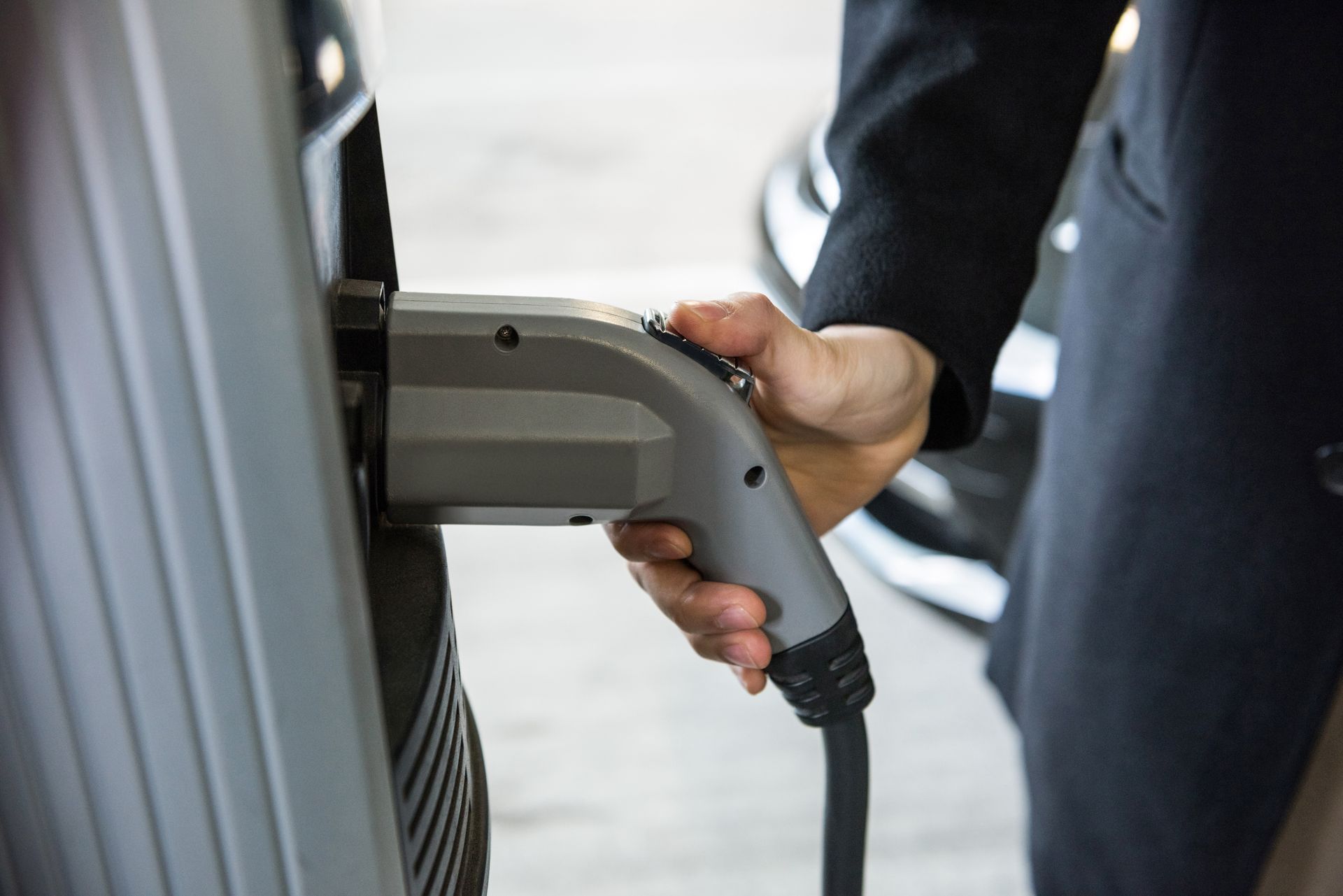 A man in a suit, plugging an electric car in charging station.