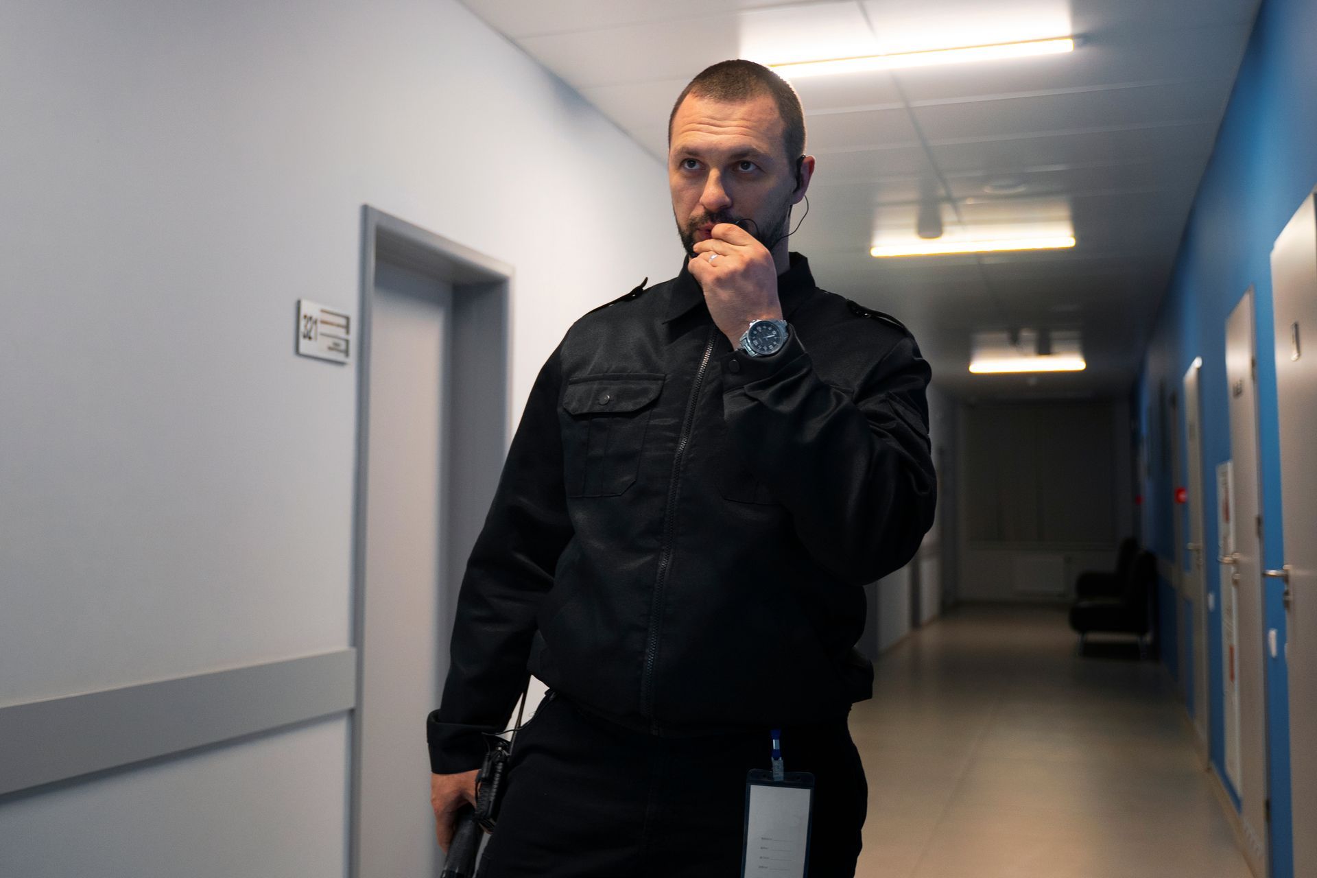 Man in black uniform in a hospital hallway, speaking into a radio.