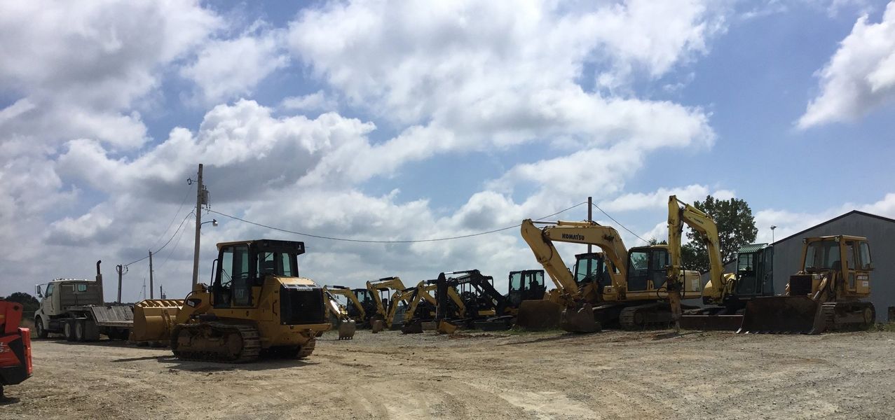 Construction equipment parked in a lot under a cloudy sky.