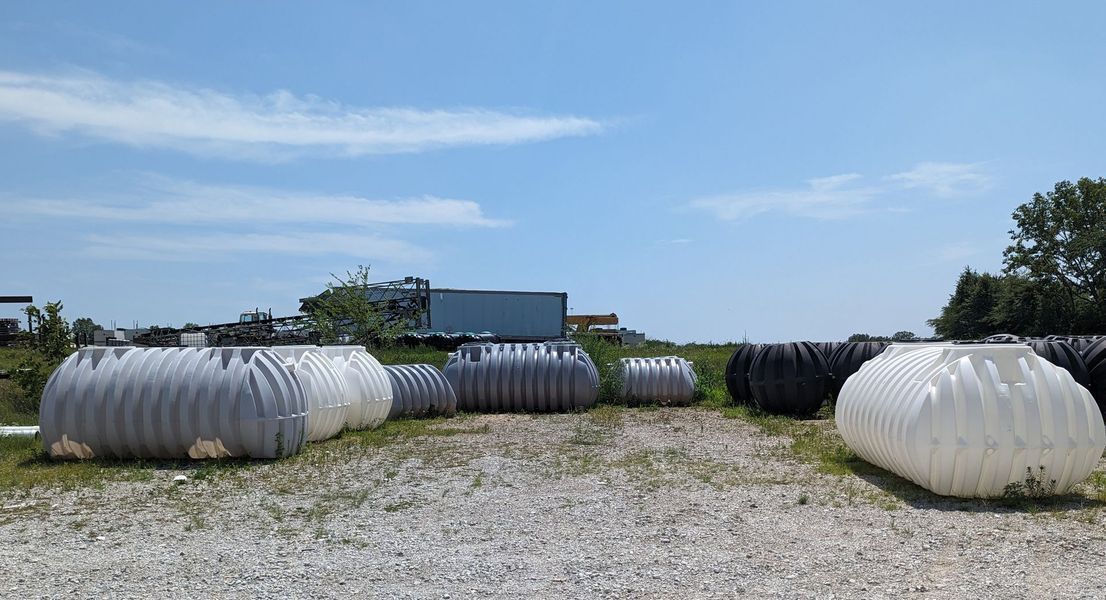 Corrugated plastic culverts in various colors on a gravel lot under a blue sky.