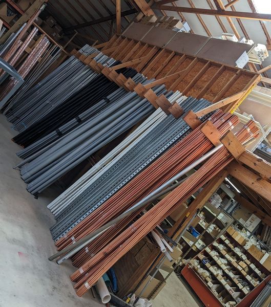 Pipes and metal rods of various colors are stacked in a wooden structure.