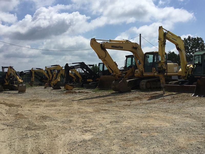 Yellow construction excavators parked outdoors on a gravel lot under a cloudy sky.