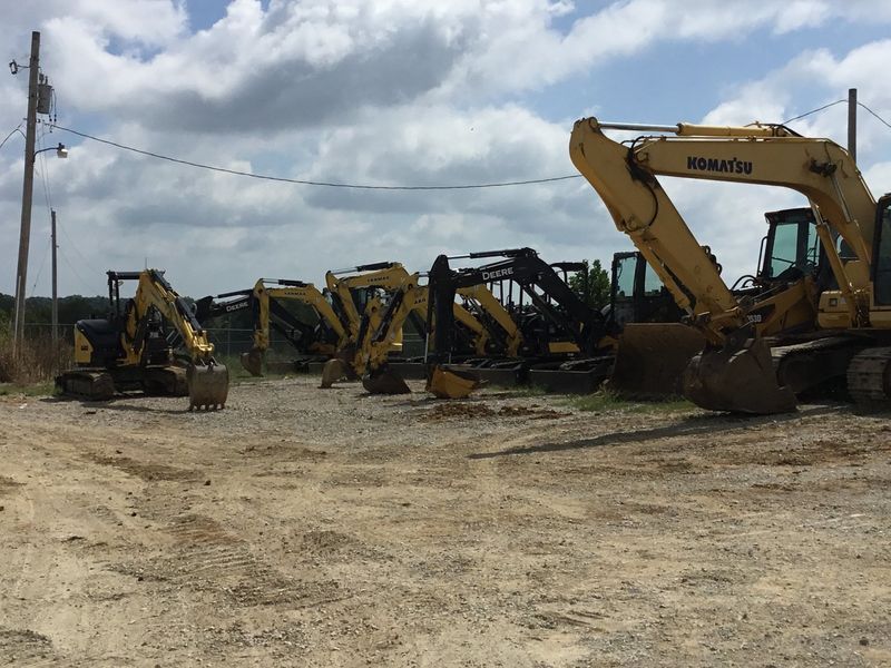 Line of yellow construction excavators parked on a gravel lot under a cloudy sky.