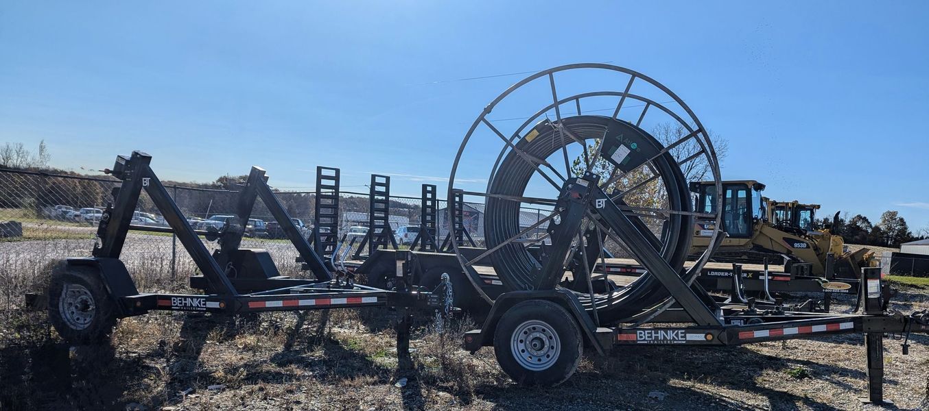 Trailer with large cable reel, parked outside on a sunny day.