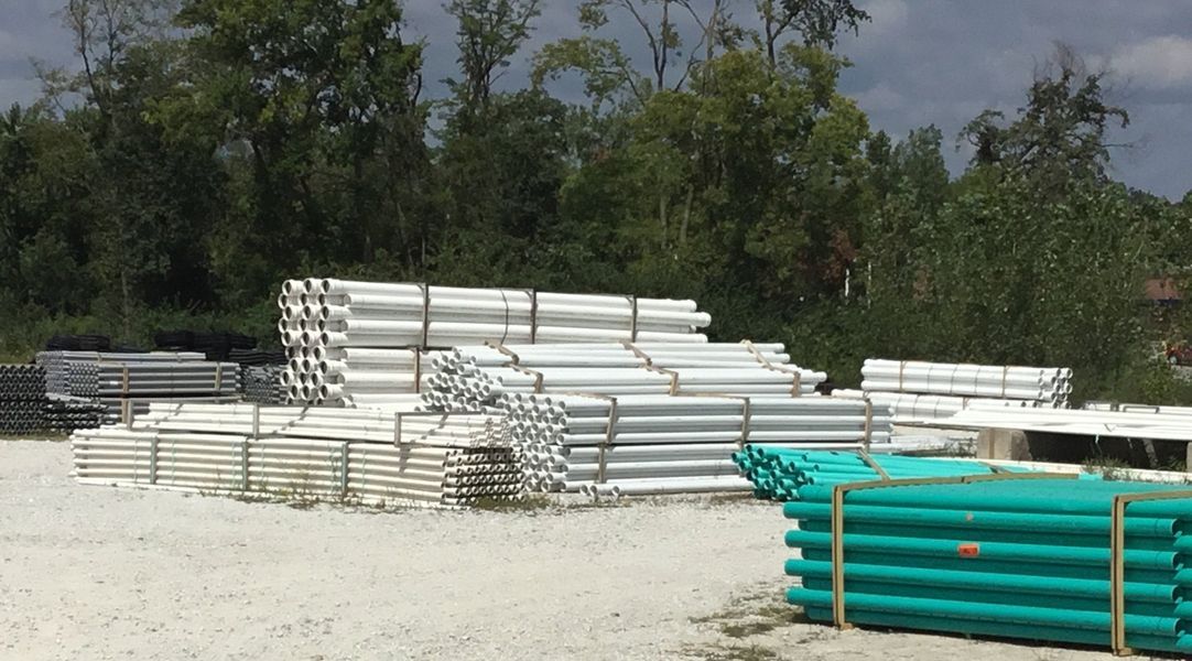Piles of metal pipes and other construction materials in an outdoor storage area. Green and silver colors dominate.