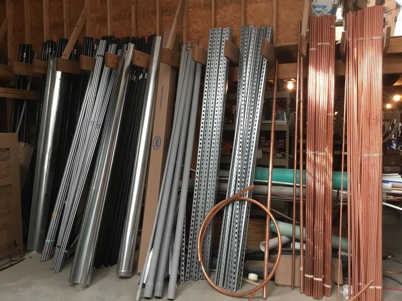 Metal pipes and copper tubing of various lengths leaned against a wooden wall in a garage.