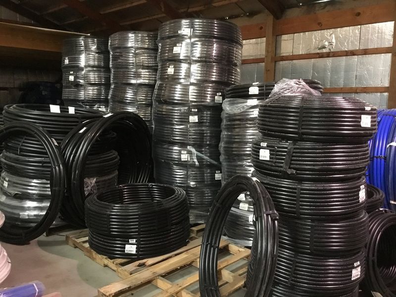 Stacks of black plastic tubing rolls on wooden pallets inside a warehouse.