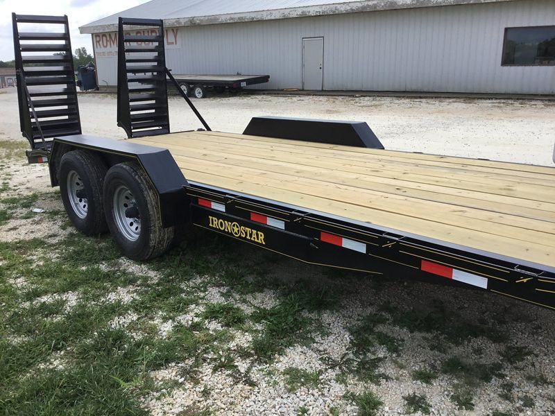 Black Iron Buster trailer with wooden deck, two axles, and loading ramps, parked outside.