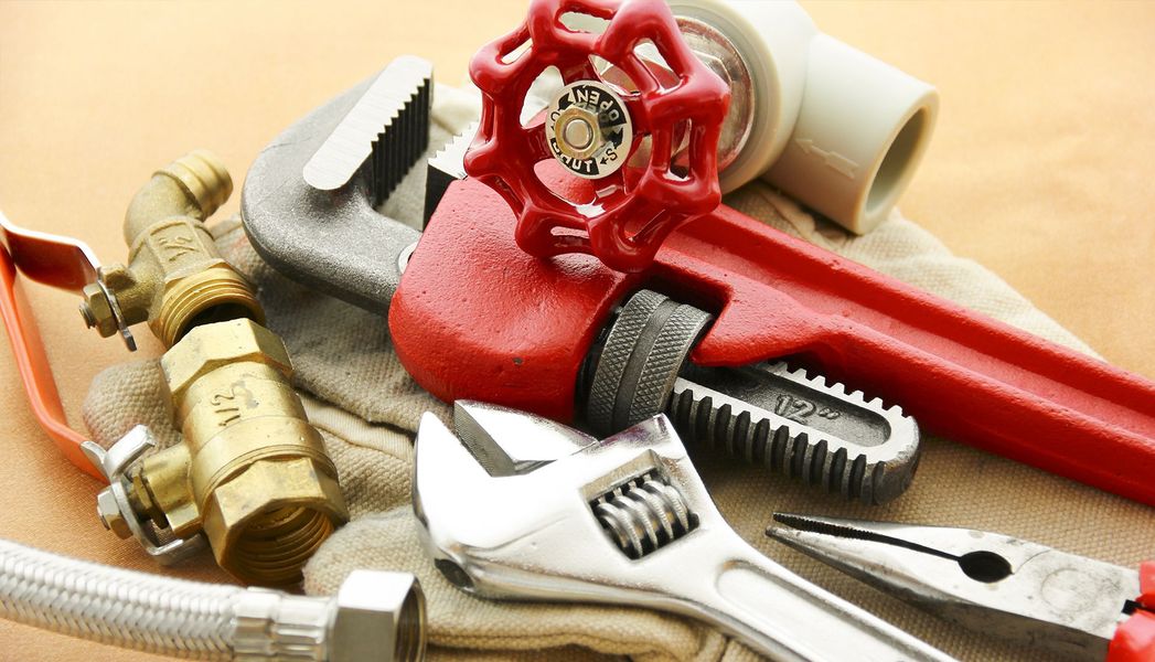 Plumbing tools and fittings, including wrenches, valves, and piping, arranged on a surface.