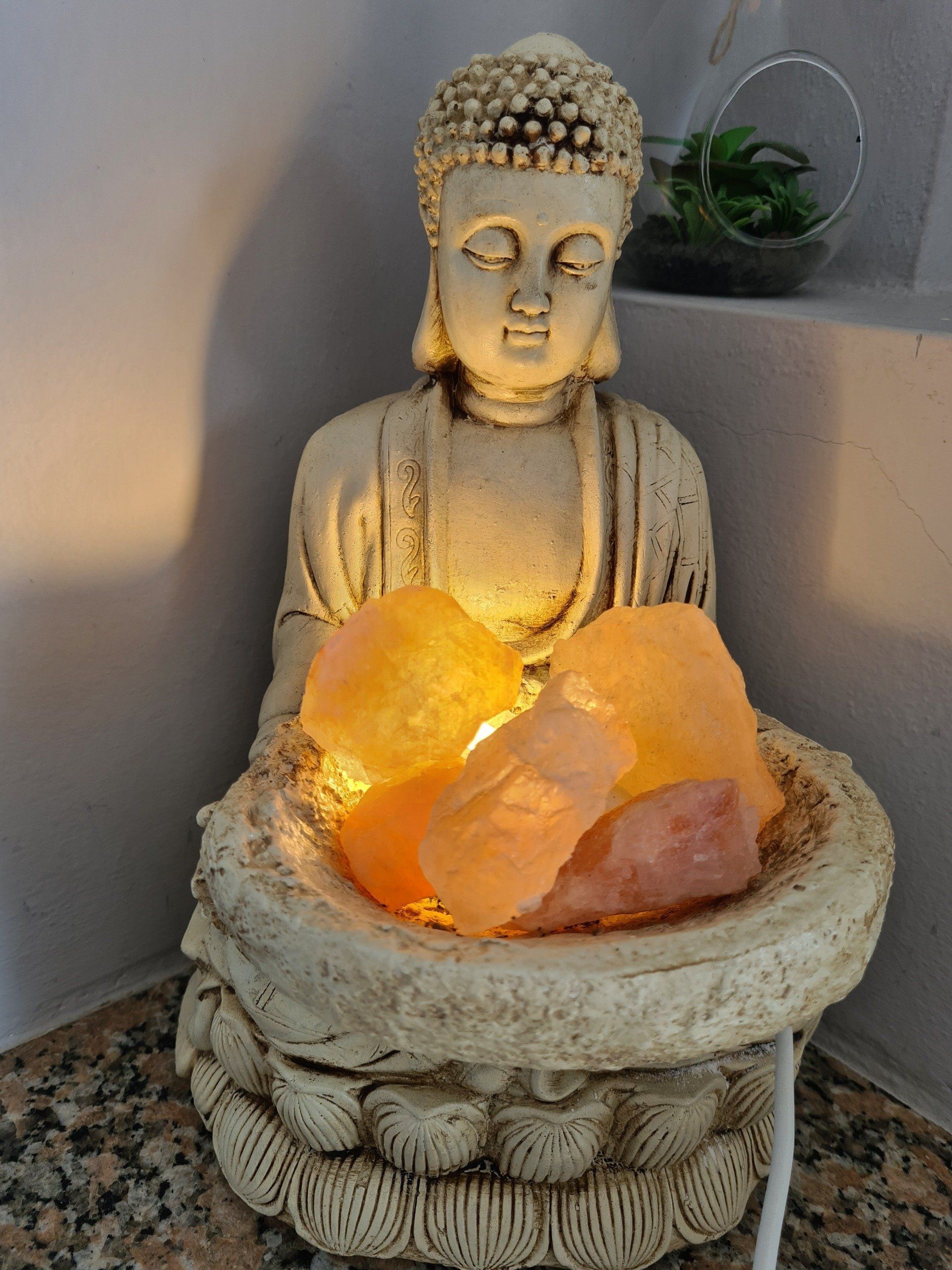 Estatua de Buda sosteniendo cristales de sal del Himalaya de color naranja brillante, iluminada, en el interior.