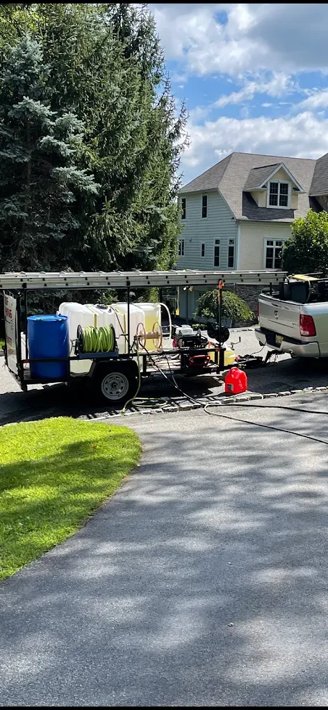 A trailer with equipment, a red cone, and a white pickup truck parked in a driveway in front of a house.