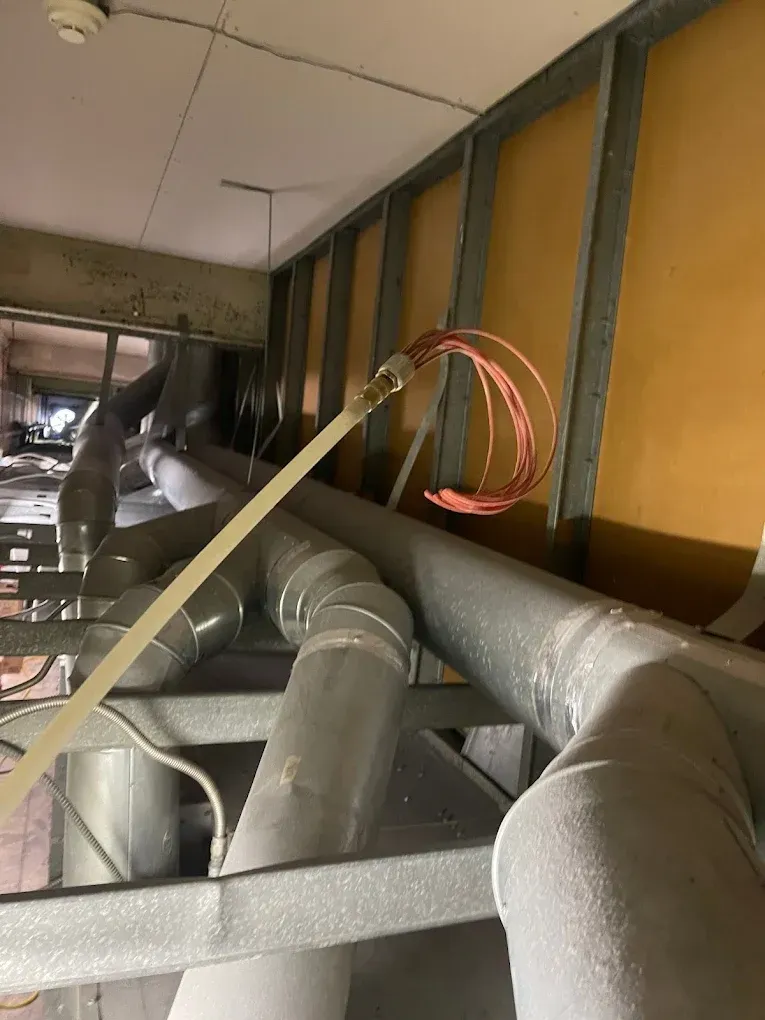 Pipes and wires in a ceiling, likely part of an HVAC system, with metal framing and insulation.