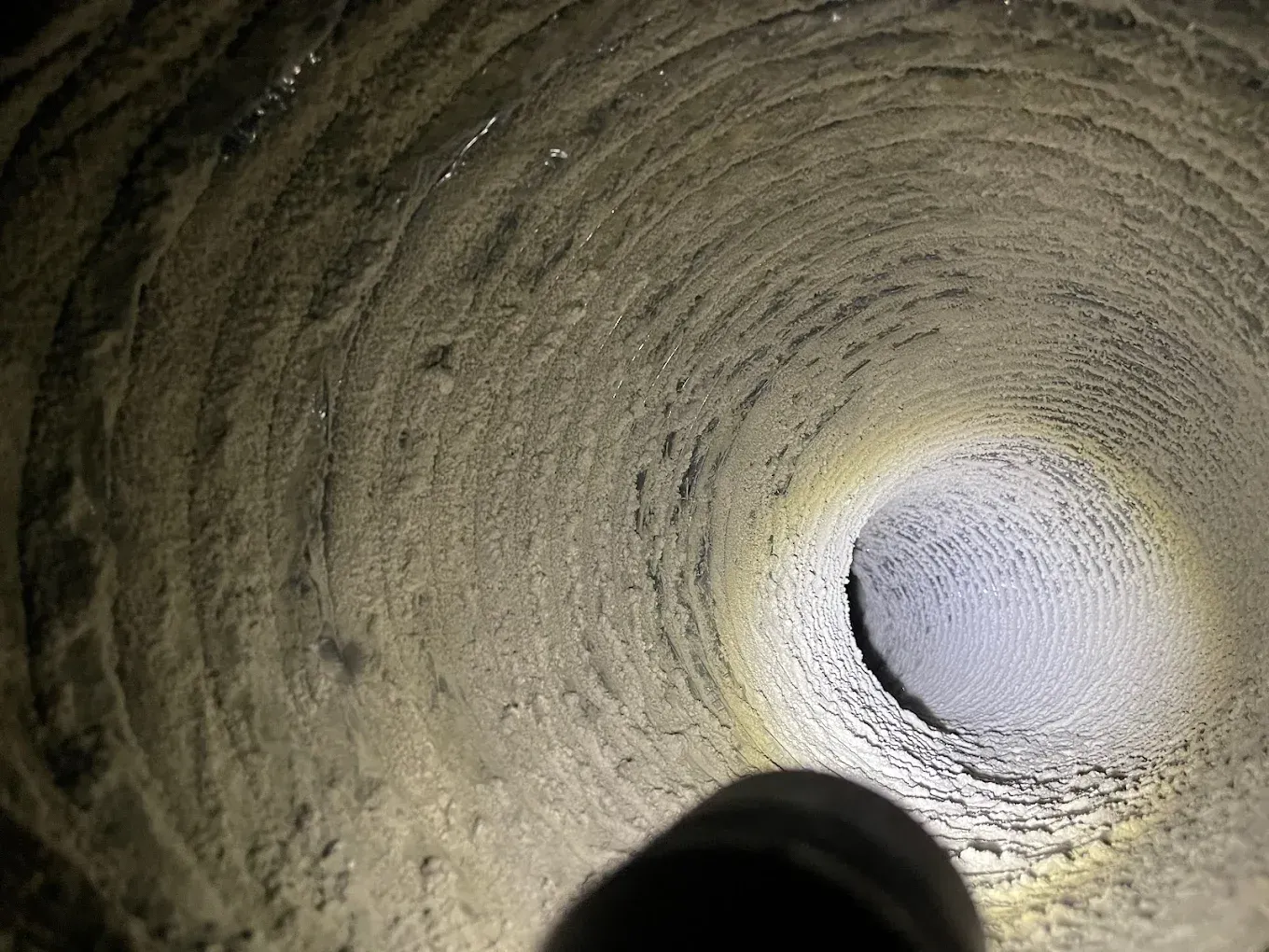 Dirty air duct interior with accumulated dust and debris illuminated by a flashlight.