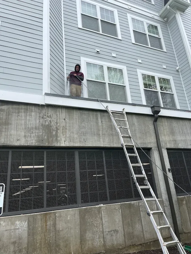 Person on a building ledge near windows; a ladder extends down to a concrete wall with grated openings.