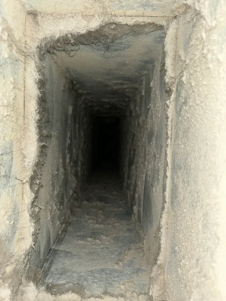 Looking down a dark, square ventilation shaft; dusty, concrete walls.