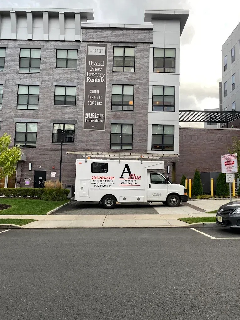 White service van parked near a brick apartment building. The building has a banner and windows.