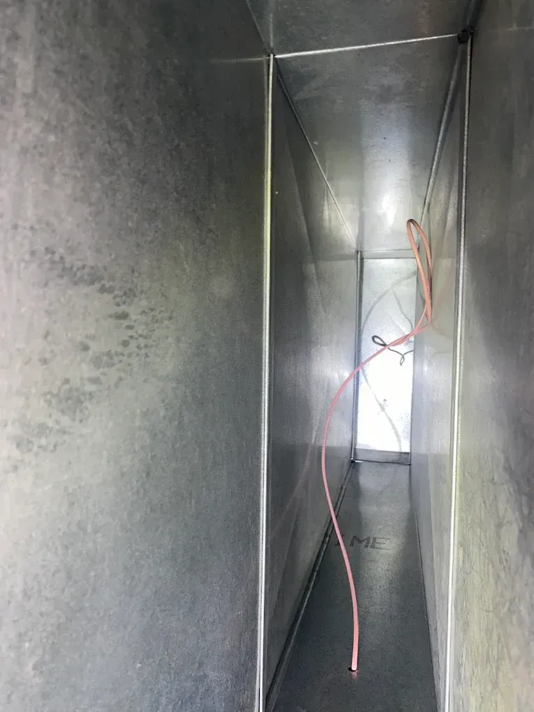 Inside a rectangular metal duct. Pink wires hang inside, running towards the end of the duct.