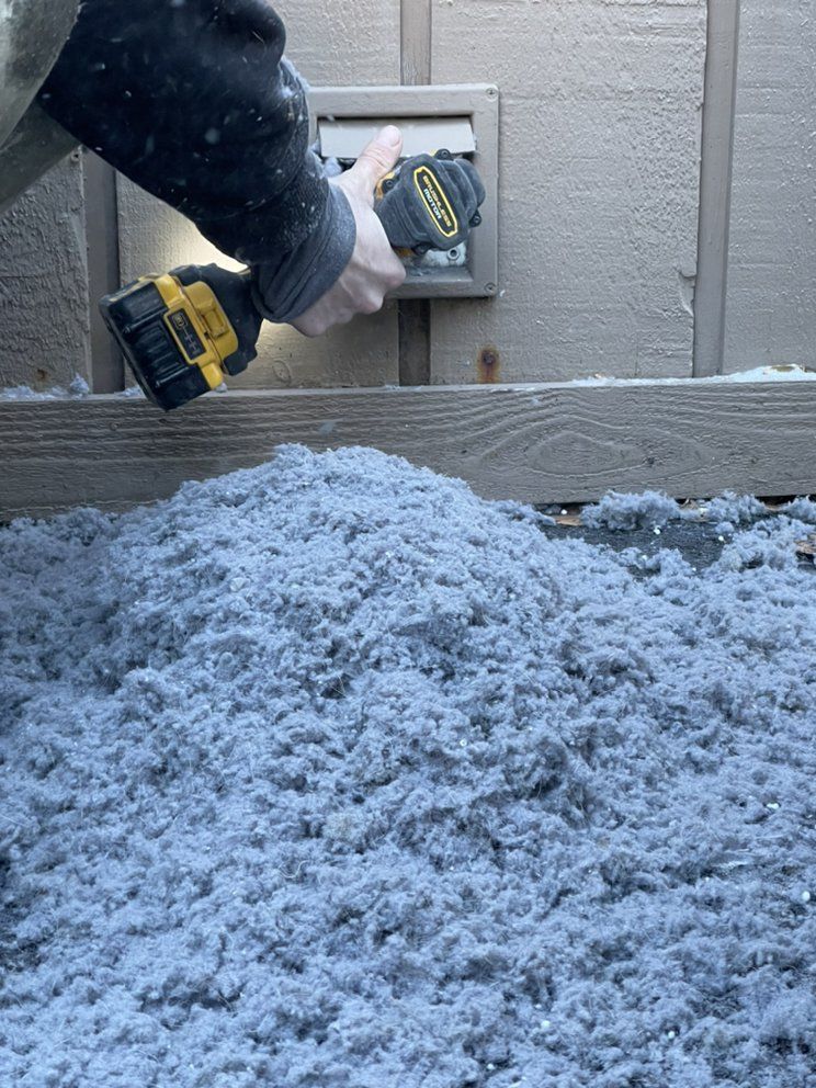 Person using a drill on a vent, with a large pile of blue-gray insulation below.