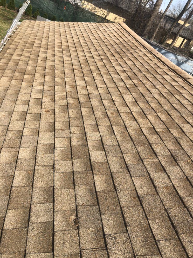 Tan shingle roof, angled view, showing texture and slight weathering. Sunlight.