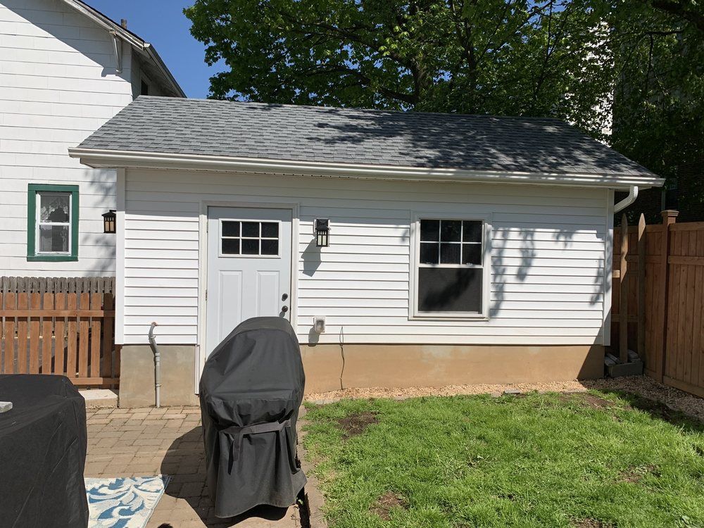 White building with door, window, and grill in backyard with green grass and brown fence.