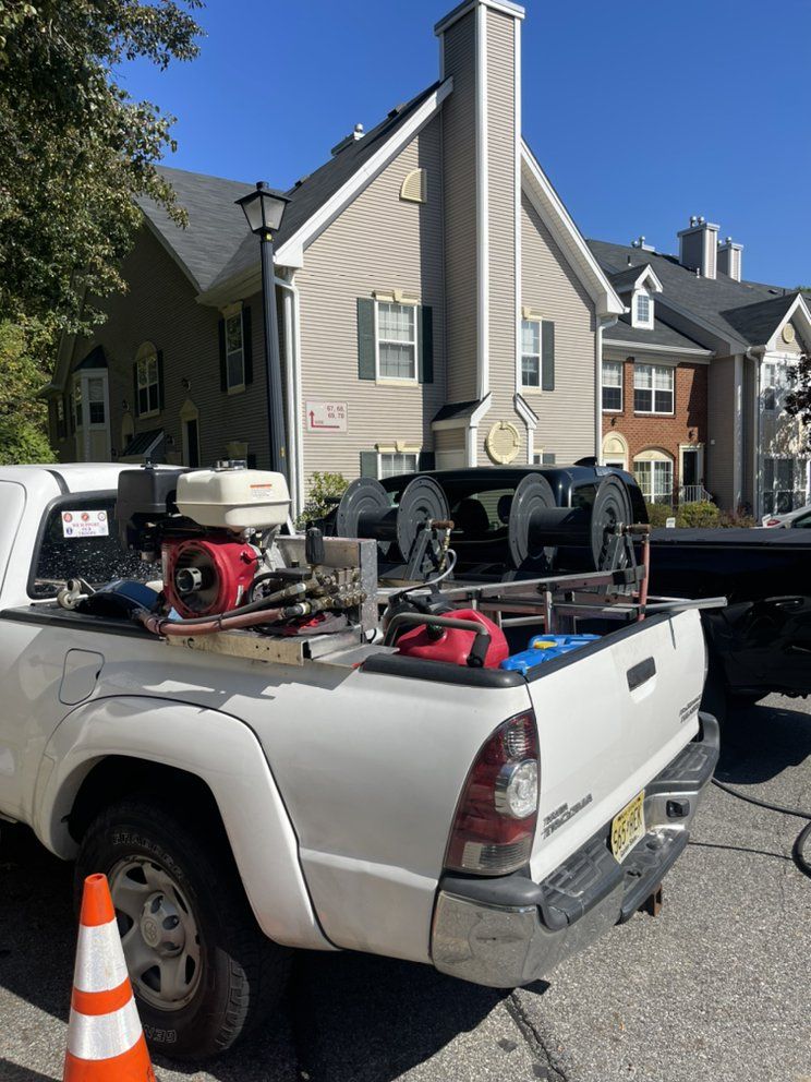 White pickup truck with equipment, parked in front of a tan apartment building, sunny day.